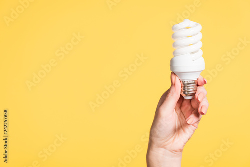 cropped view of female hand holding fluorescent lamp isolated on yellow, energy efficiency concept