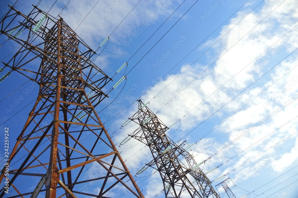 Power transmission line pylons with threatening blue clouds background