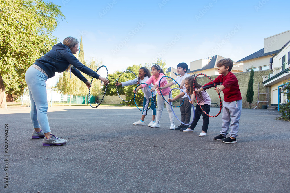 Obraz premium Sportlehrer zeigt Kindern Übung mit Reifen