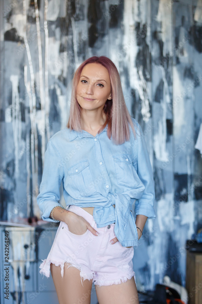 Naklejka premium Attractive young charming woman posing on a gray-blue background in summer clothes. Sexy young female female student posing in studio in denim clothes