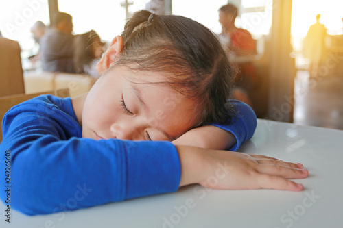 Tired little Asian child girl sleeping on white table at cafe.