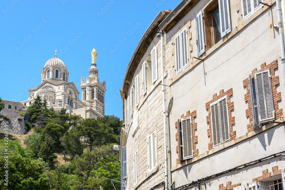 Rear view of Notre-Dame de la Garde basilica on top of the hill in Marseille, France, seen from the street below with old townhouses in the foreground.