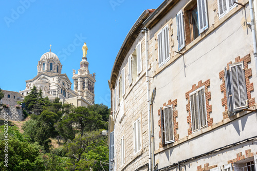 Rear view of Notre-Dame de la Garde basilica on top of the hill in Marseille, France, seen from the street below with old townhouses in the foreground. © olrat