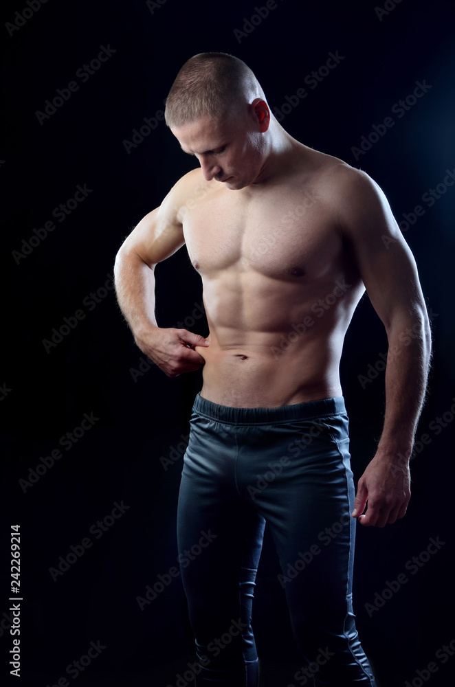 Athletic fitness young guy showing perfect abdominal muscle on a black studio background. Athletic fitness young guy showing perfect abdominal muscle on a black studio background.
