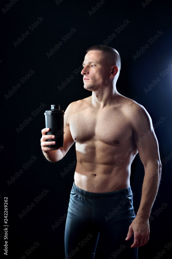 Athletic brawny sportman holds a black shaker with protein on the dark background. Athletic brawny sportman holds a black shaker with protein on the dark background.