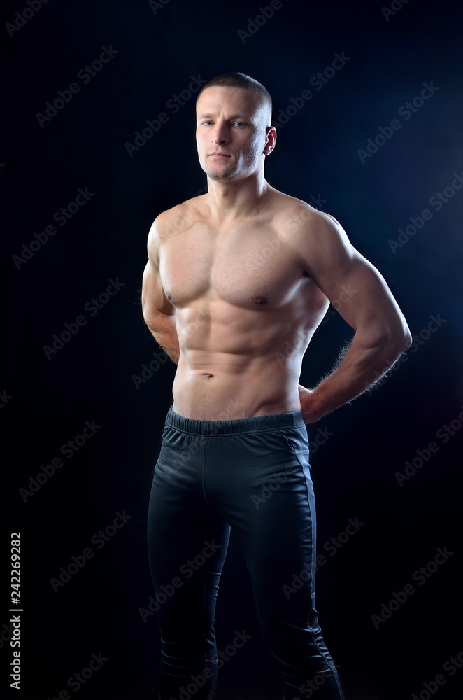Athletic brawny trainer posing with chest and back muscles on a black studio background