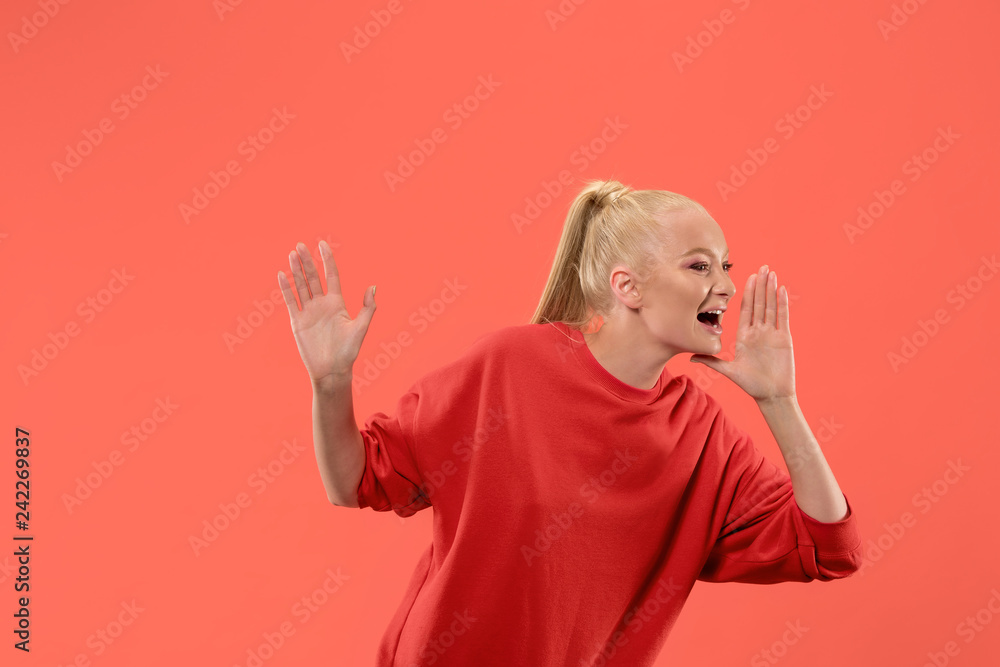 Do not miss. Young casual woman shouting. Shout. Crying emotional woman screaming on coral studio background. Female half-length portrait. Human emotions, facial expression concept. Trendy colors