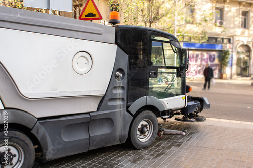 Street sweeper machine washing city street during sunny day in the middle of the road