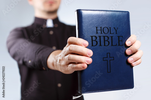 Young priest holding the Holy Bible on neutral background