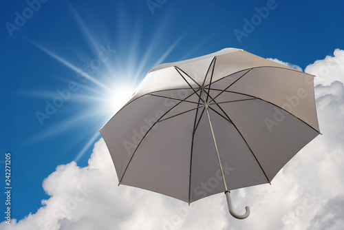 Umbrella on a blue sky with clouds and sun rays