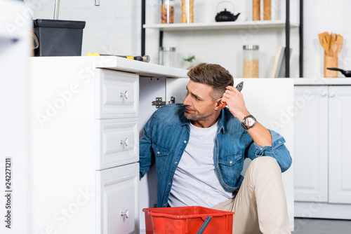 confused man sitting on floor while repairing kitchen sink
