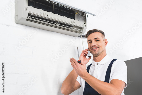 happy man talking on smartphone while repairing air conditioner