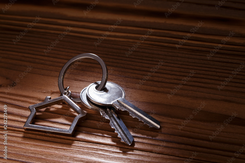 House keys with house shaped keychain on wooden background House keys with house shaped keychain on wooden background