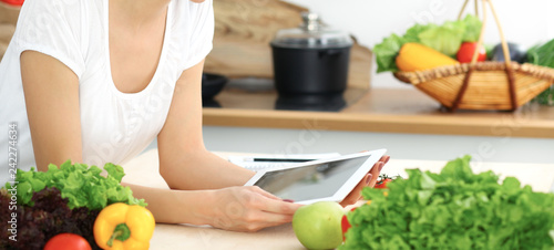 Beautiful Hispanic woman cooking while using tablet computer in kitchen or making online shopping by touchpad and credit card. Housewife found new recipe for dinner