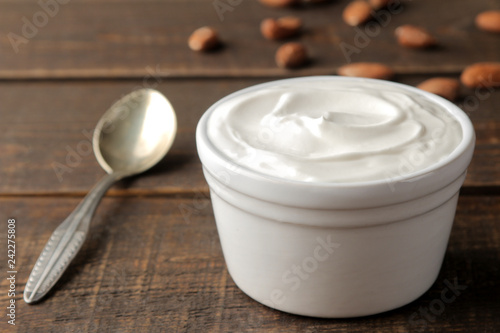 Greek yogurt in a ceramic bowl and with almond nut next to a spoon on a brown wooden background.