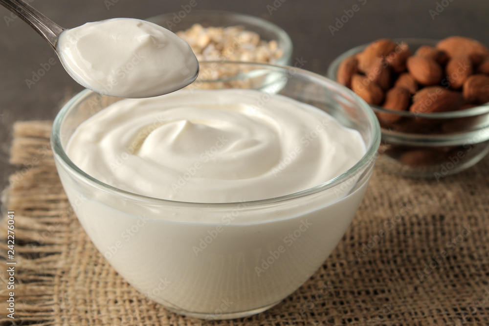 Greek yogurt in a glass bowl next to a spoon, oatmeal and almonds on a dark background. healthy food. natural yoghurt. breakfast Greek yogurt in a glass bowl next to a spoon, oatmeal and almonds on a dark background. healthy food. natural yoghurt. breakfast