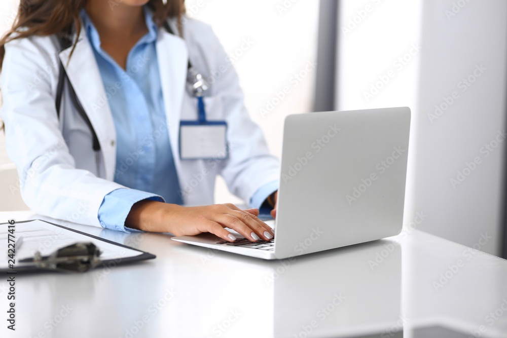 Unknown doctor woman typing on laptop computer while sitting at the desk in hospital office. close-up of hands. Physician at work. Medicine and health care concept Unknown doctor woman typing on laptop computer while sitting at the desk in hospital office. close-up of hands. Physician at work. Medicine and health care concept