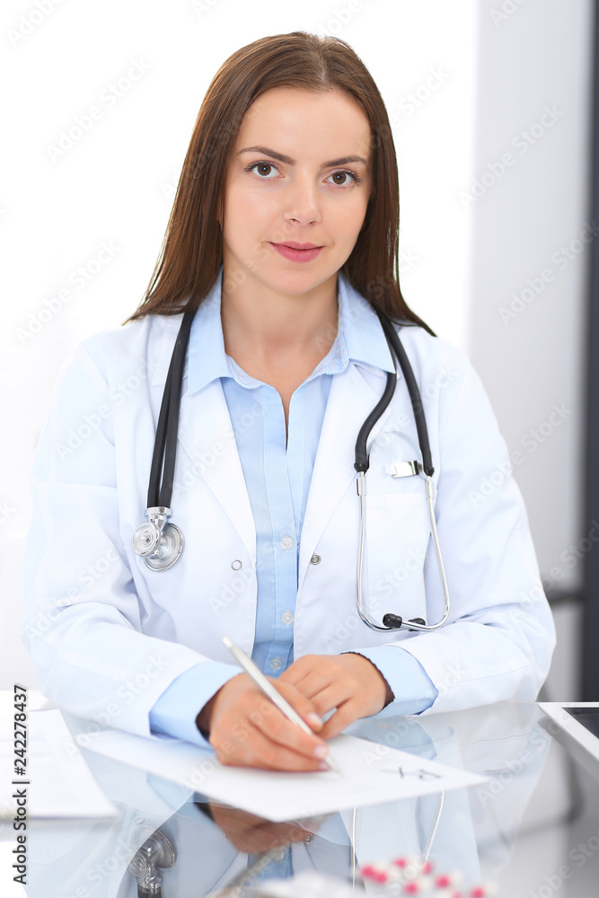 Doctor woman at work. Portrait of female physician filling up medical form while sitting at the glass desk at clinic or hospital. Medicine and healthcare concept Doctor woman at work. Portrait of female physician filling up medical form while sitting at the glass desk at clinic or hospital. Medicine and healthcare concept