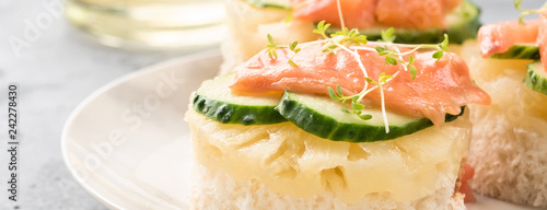 Bruschetta toast of white bread with slices of pineapple cucumber fish salmon and fresh green sprouts. Served on a white plate on table with mineral water olive oil