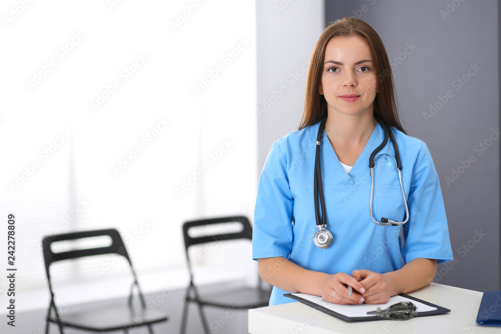 Doctor woman at work. Portrait of female physician filling up medical form while standing near reception desk at clinic or emergency hospital. Medicine and healthcare concept Doctor woman at work. Portrait of female physician filling up medical form while standing near reception desk at clinic or emergency hospital. Medicine and healthcare concept