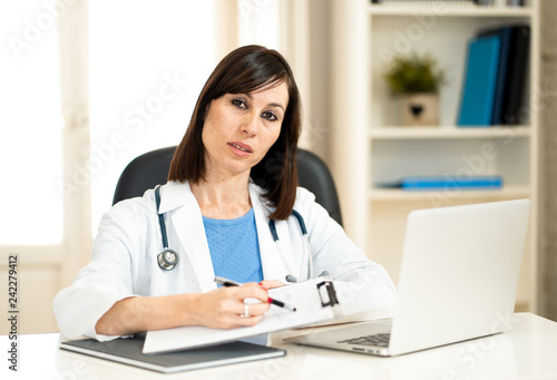 Female doctor working with stethoscope and clipboard in medical office with serious face expression
