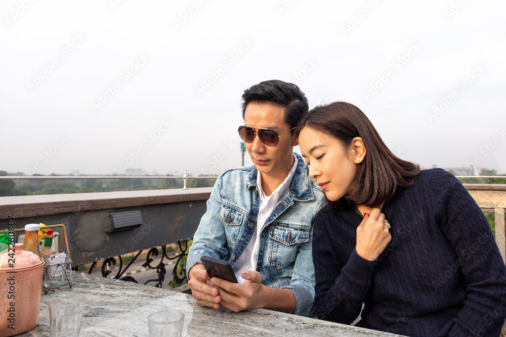 Asian couple looking at cellphone on outdoor cafe.