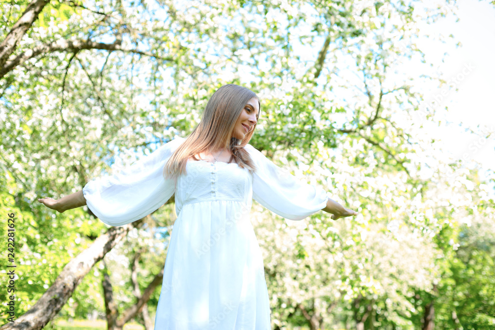 Happy blonde woman on a background of blooming spring garden with her hands raised to the sky Happy blonde woman on a background of blooming spring garden with her hands raised to the sky