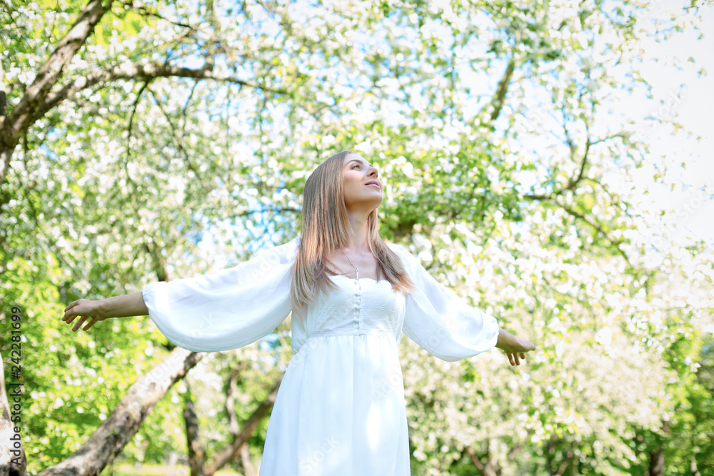 Happy blonde woman on a background of blooming spring garden with her hands raised to the sky Happy blonde woman on a background of blooming spring garden with her hands raised to the sky