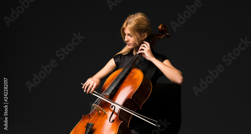 Fotografie Young girl playing the cello on isolated black background