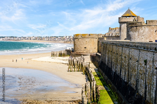 The city of Saint-Malo in Brittany seen from the surrounding wall of the old town with the towers of the castle, the breakwater made of wooden posts and the beach of L'Eventail on a sunny day.