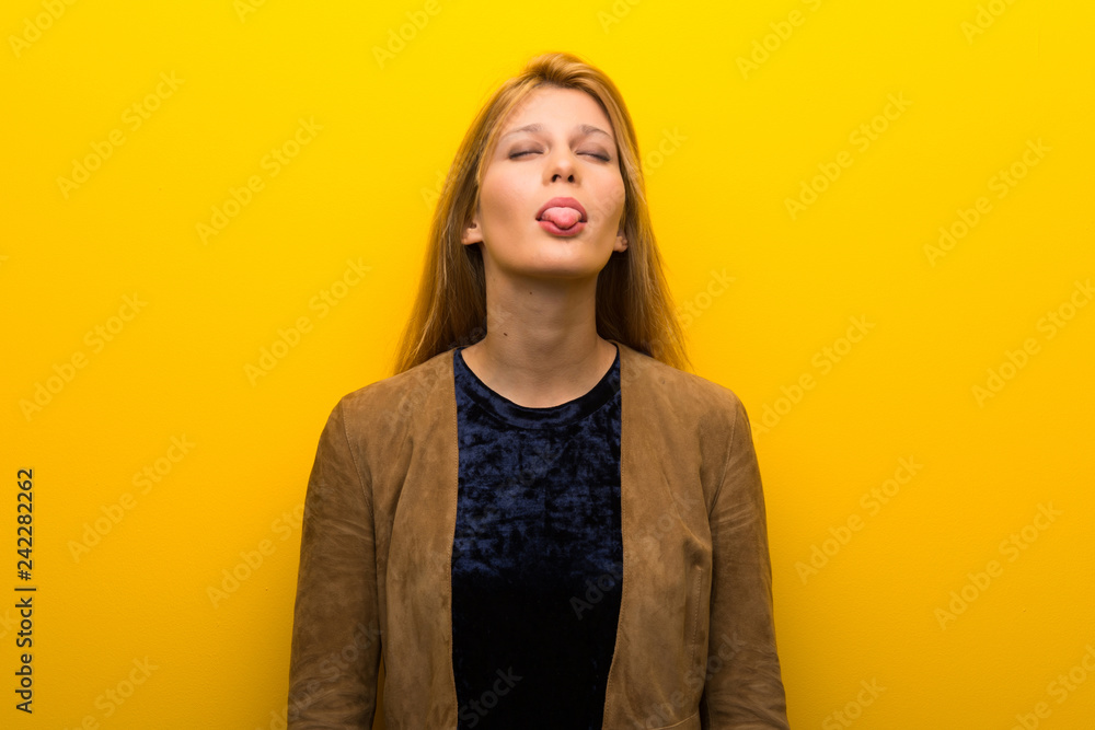 Obraz premium Blonde girl on vibrant yellow background showing tongue at the camera having funny look