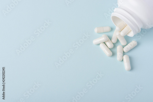 Pills capsules with white powder in white plastic bottle spill on blue background with copy-space