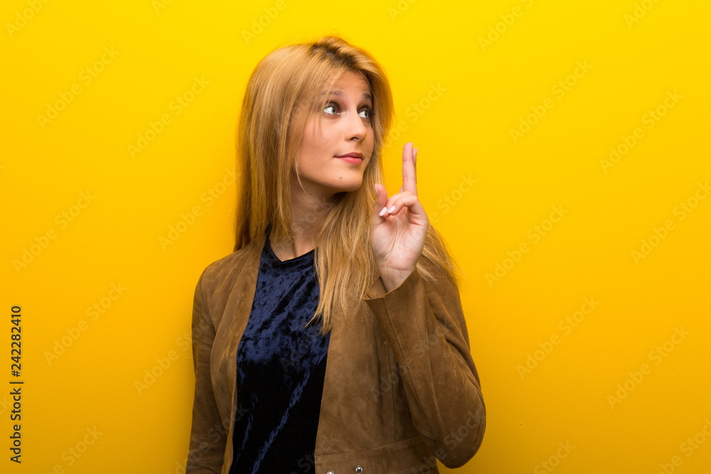 Blonde girl on vibrant yellow background with fingers crossing and wishing the best Blonde girl on vibrant yellow background with fingers crossing and wishing the best