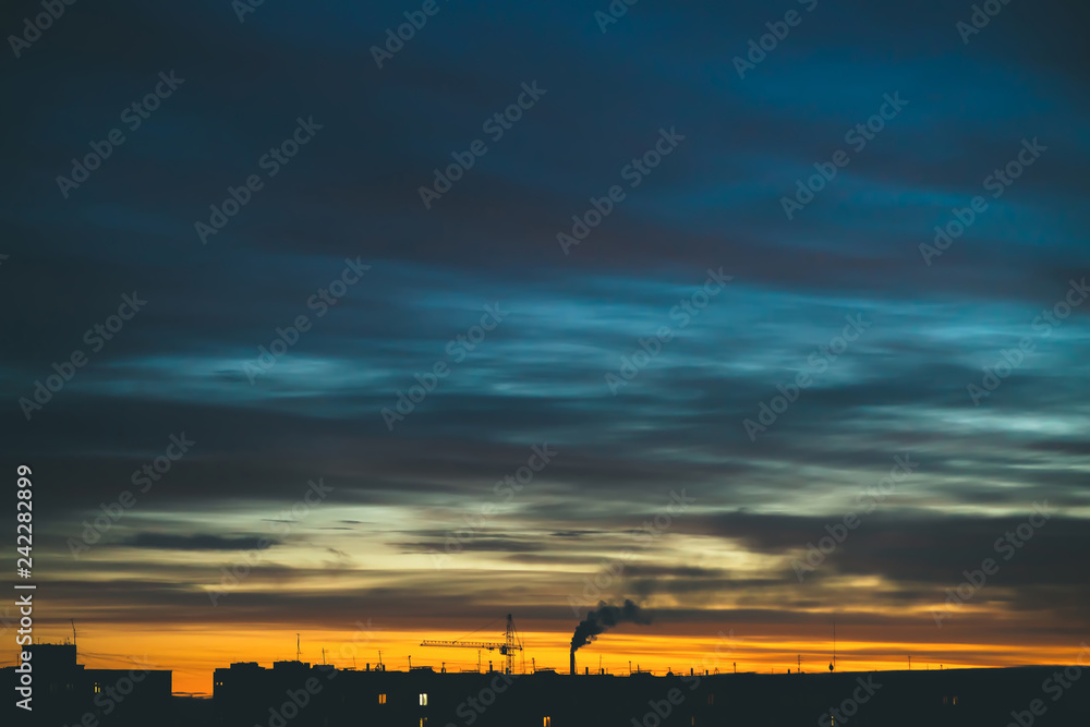 Cityscape with wonderful varicolored vivid dawn. Amazing dramatic blue cloudy sky above dark silhouettes of city buildings. Atmospheric background of orange sunrise in overcast weather. Copy space.