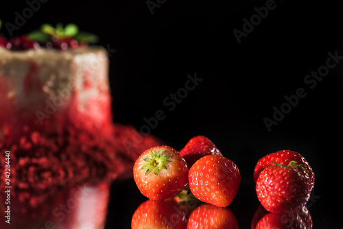 selective focus of white cake decorated with red currants and mint leaves near strawberries isolated on black