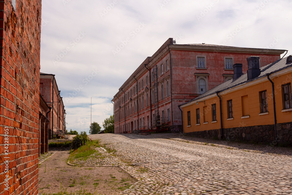 Old cobblestone road and old military buildings on the island-fort Suominlinna Sveaborg in Finland on a summer day.