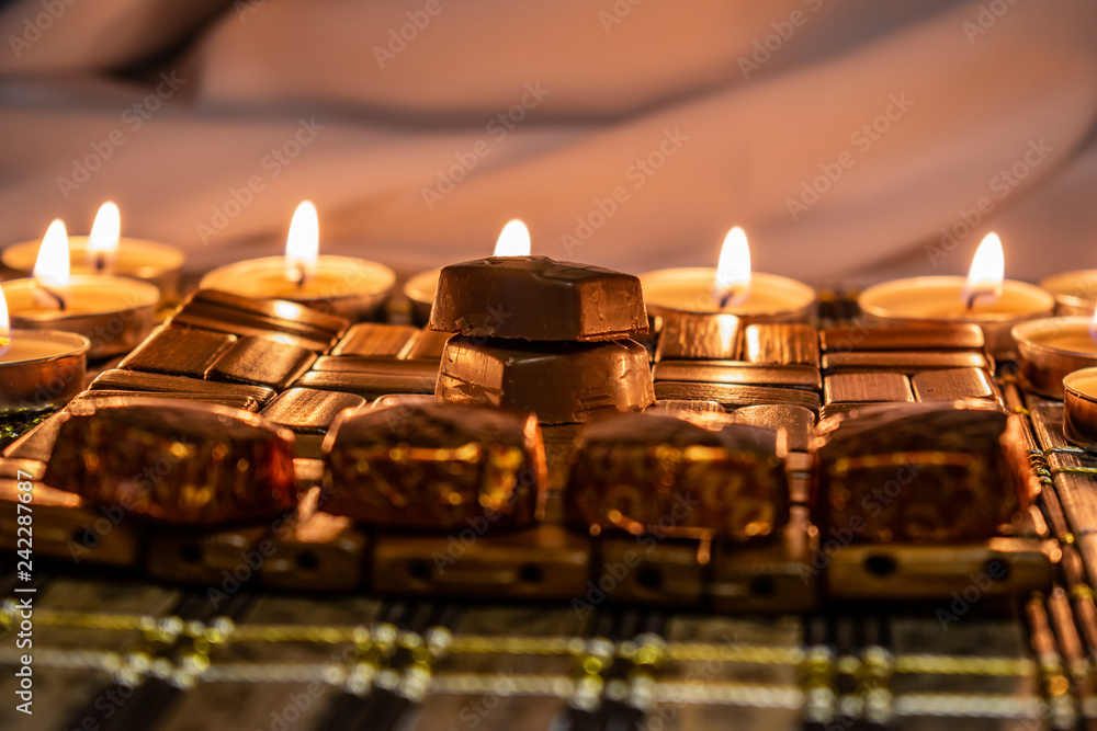 Sweets, milk candies and dark chocolate broken, on the background of lights, candles. Warm, soft and pleasant shade. Dessert is gentle and natural in a romantic home environment.