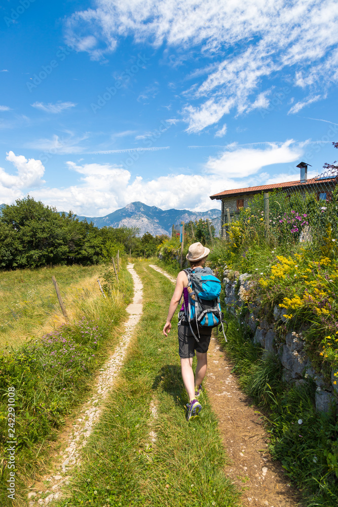 Young woman is hiking in the nature: idyllic hiking path, green grass and flowers