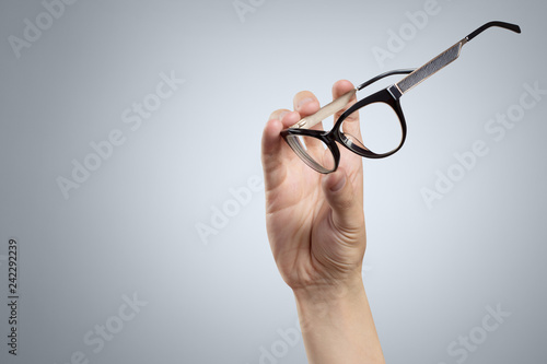 Hand holding plastic black glasses on grey background