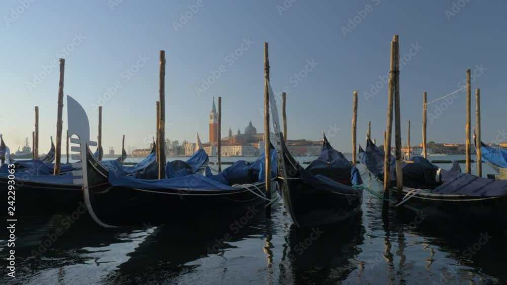 Gondolas moored at wooden piles and swinging on water. Venice scene with Church of San Giorgio Maggiore and Bell Tower in background, Italy Gondolas moored at wooden piles and swinging on water. Venice scene with Church of San Giorgio Maggiore and Bell Tower in background, Italy