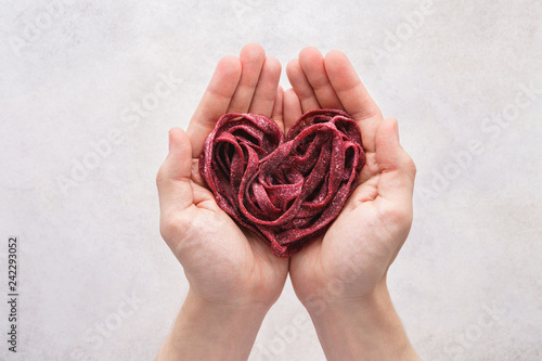 Heart made of beetroot vegetable pasta in hands. Healthy food.