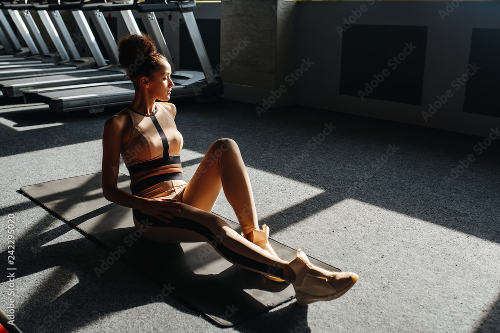 Sports fashion. Cute woman in sportswear relaxing after training. Woman looking away while sitting after workout exercise at sports gym.