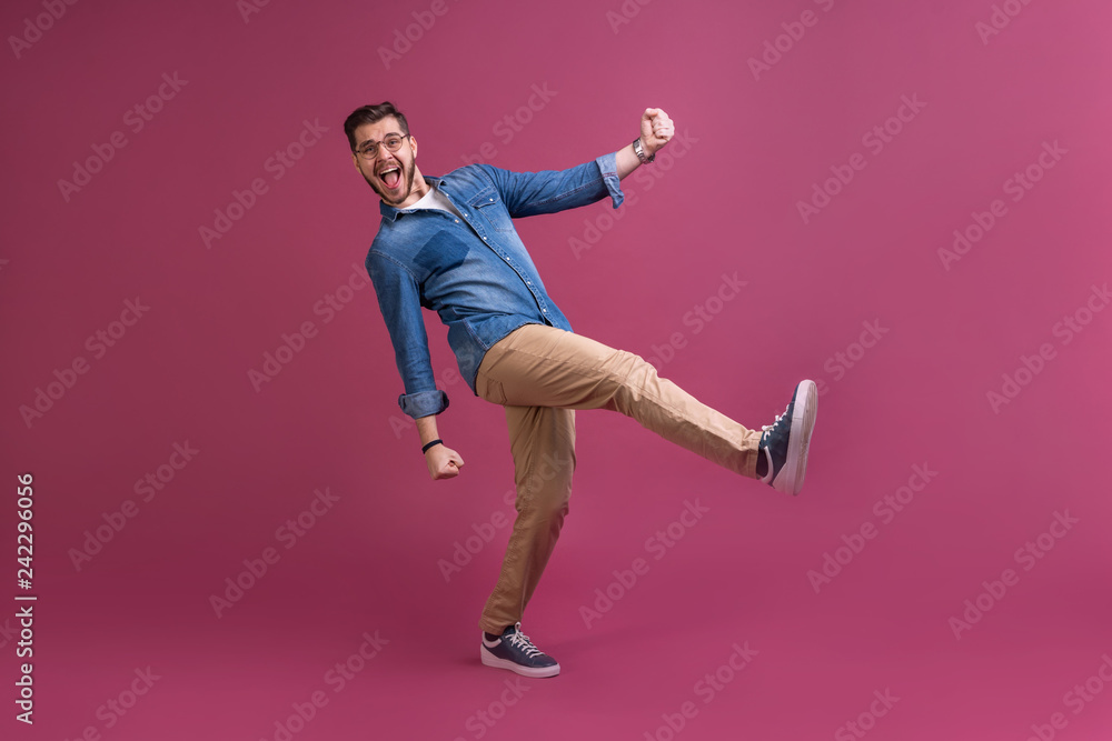 Funny man in casual is having some fun. He is posing and dancing. Isolated on pink background.