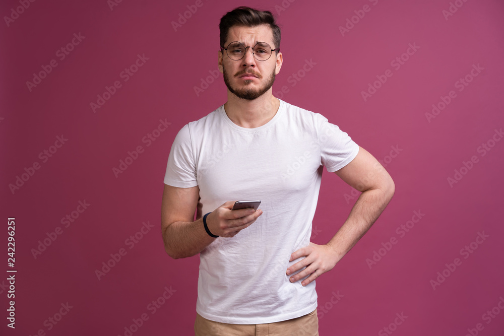 Always in touch. Smiling young man holding smart phone and looking at it. Portrait of a happy man using mobile phone isolated over pink background Always in touch. Smiling young man holding smart phone and looking at it. Portrait of a happy man using mobile phone isolated over pink background