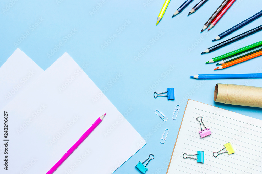 Wooden colored pencils, clean school notebook in line, paper clips on blue background top view flat lay copy space. Pencils for drawing, objects for creativity. Back to school concept. Wooden colored pencils, clean school notebook in line, paper clips on blue background top view flat lay copy space. Pencils for drawing, objects for creativity. Back to school concept.