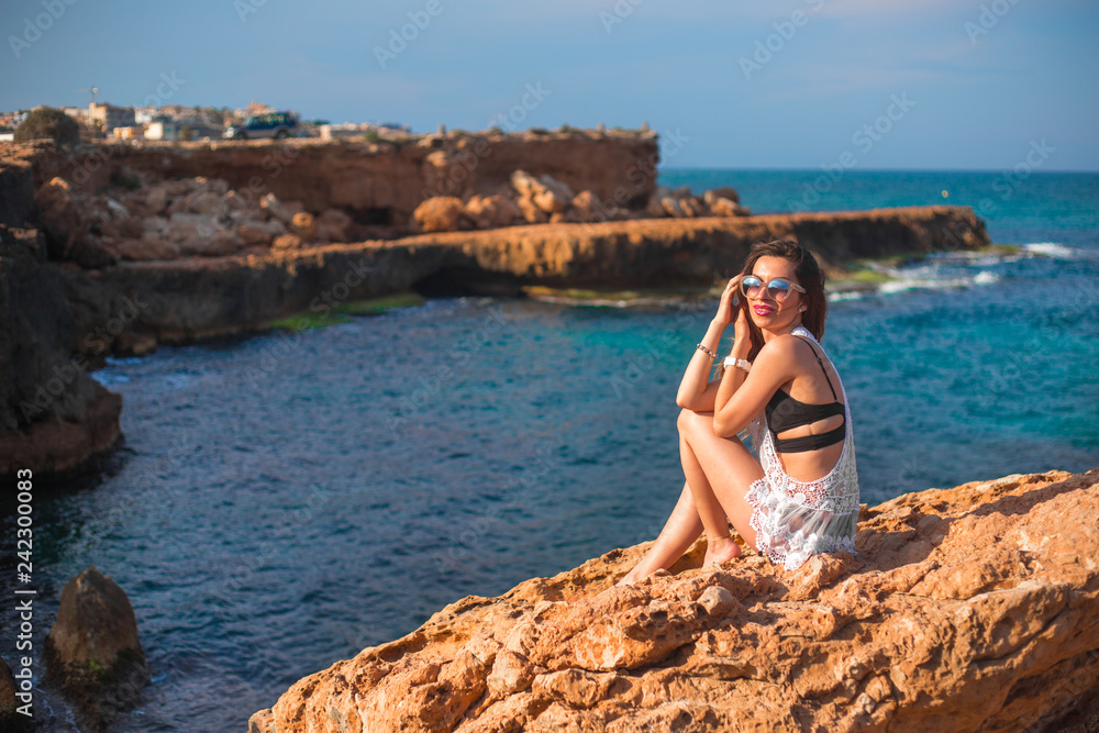 Model sitting on edge of rocks with sea view 