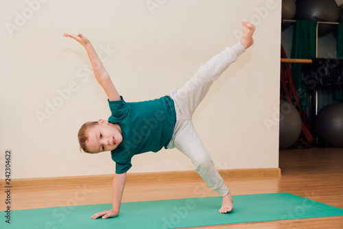 Cute little boy is learning to do yoga in the gym