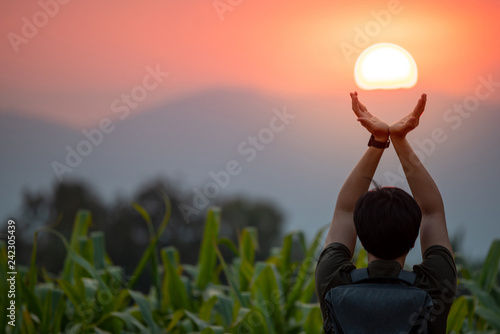 Asian man in corn field raising his arms holding the sun at sunset. Hope and pray. Achievement concept