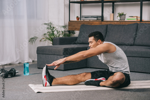 mixed race man doing stretching exercise on fitness mat in living room