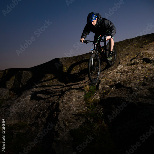 Cyclist Riding the Bike on Rocky Trail at Night. Extreme Sport and Enduro Biking Concept.